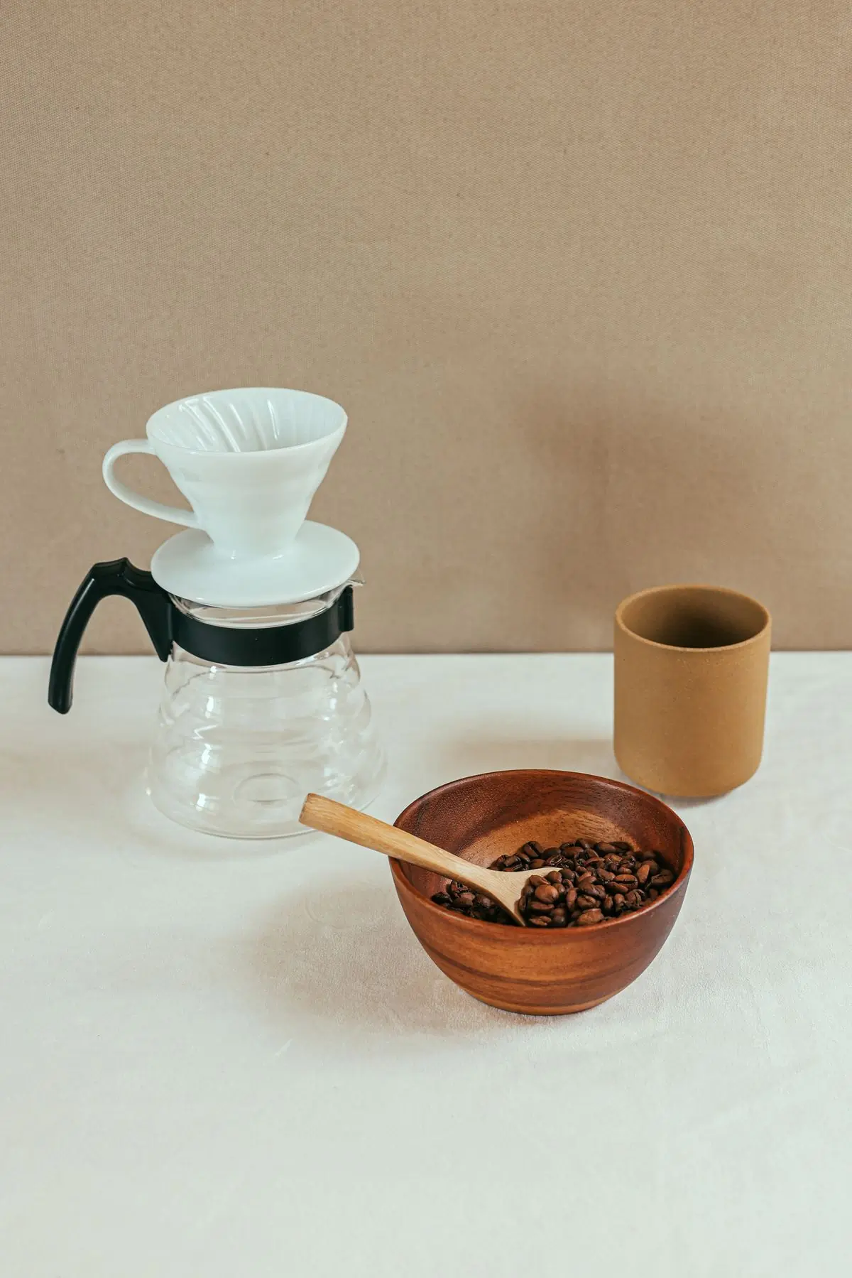 A white ceramic pour-over cone on its glass carafe, beside a bowl of beans