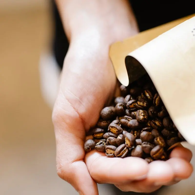 Roasted beans poured from a kraft bag into an open hand
