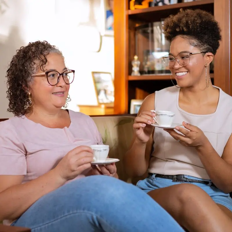 Two women talking over cups of coffee in front of a warm wooden cabinet