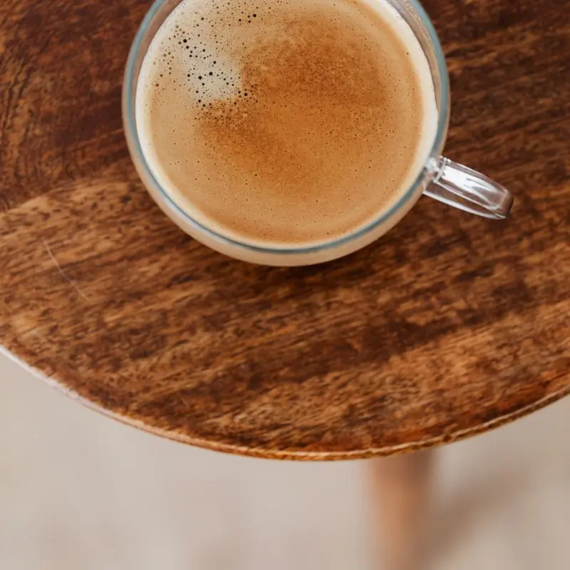A cappuccino in a glass cup on a round wooden table, seen from above