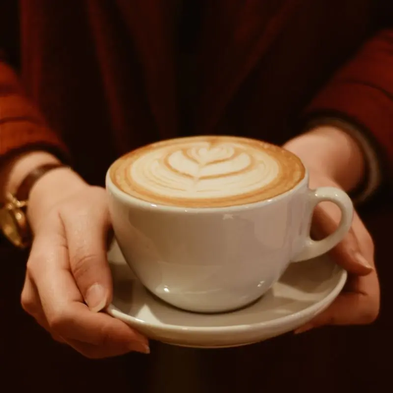 A flat white on a saucer being carried out to a table