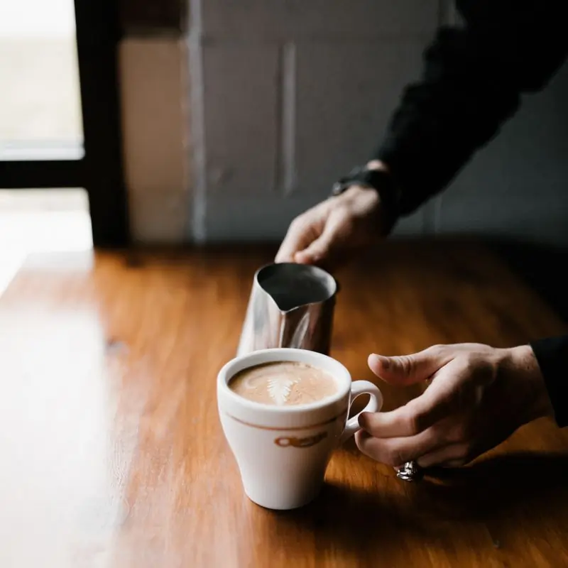 A barista pouring milk into a cup on a wooden counter