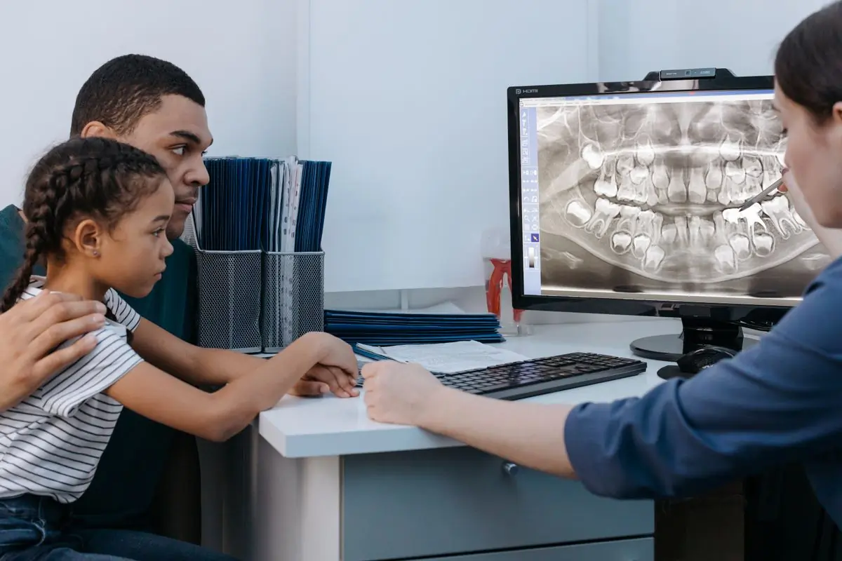 A dentist showing a patient and their child an x-ray on screen