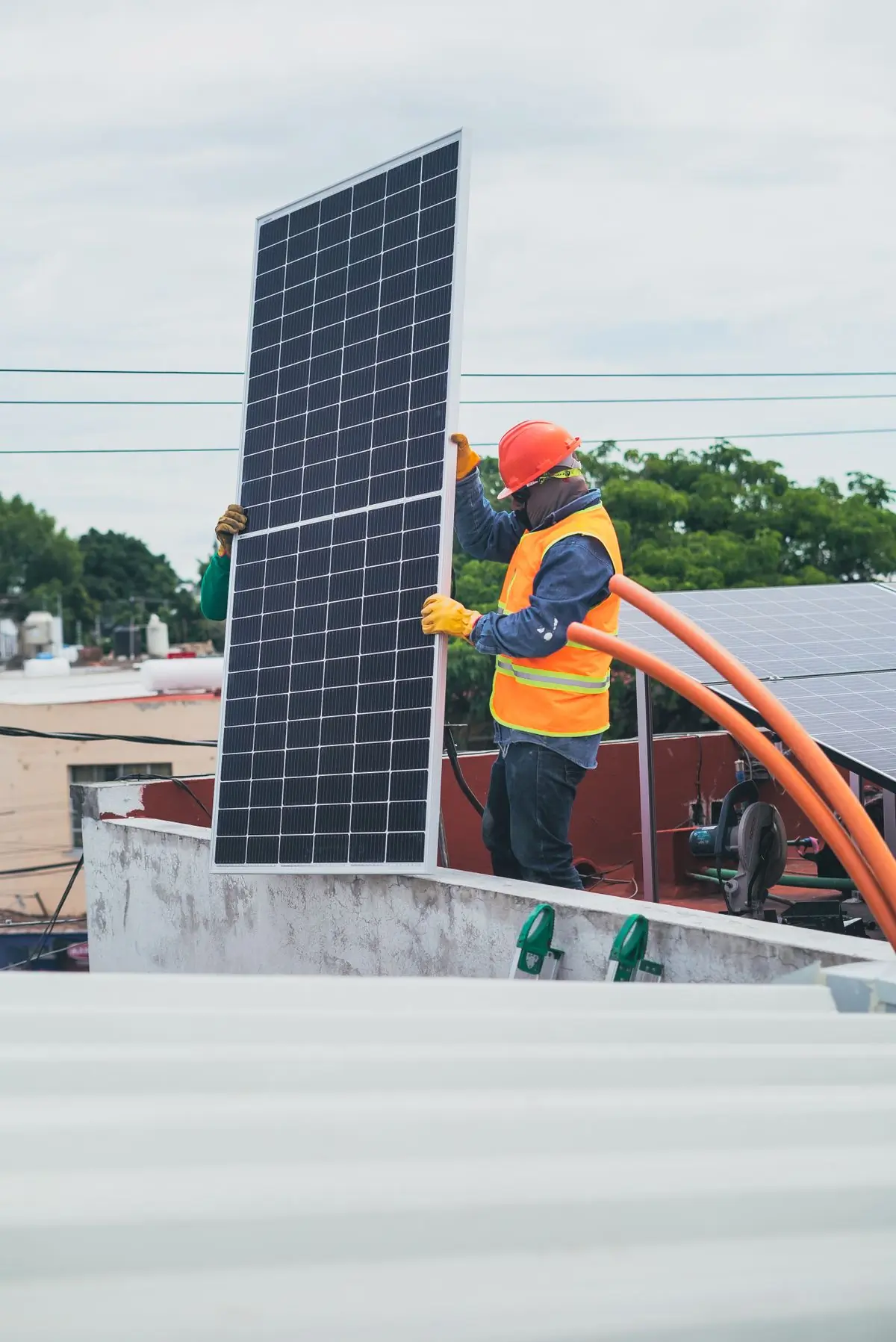 A worker in high-visibility clothing carrying a solar panel across a rooftop