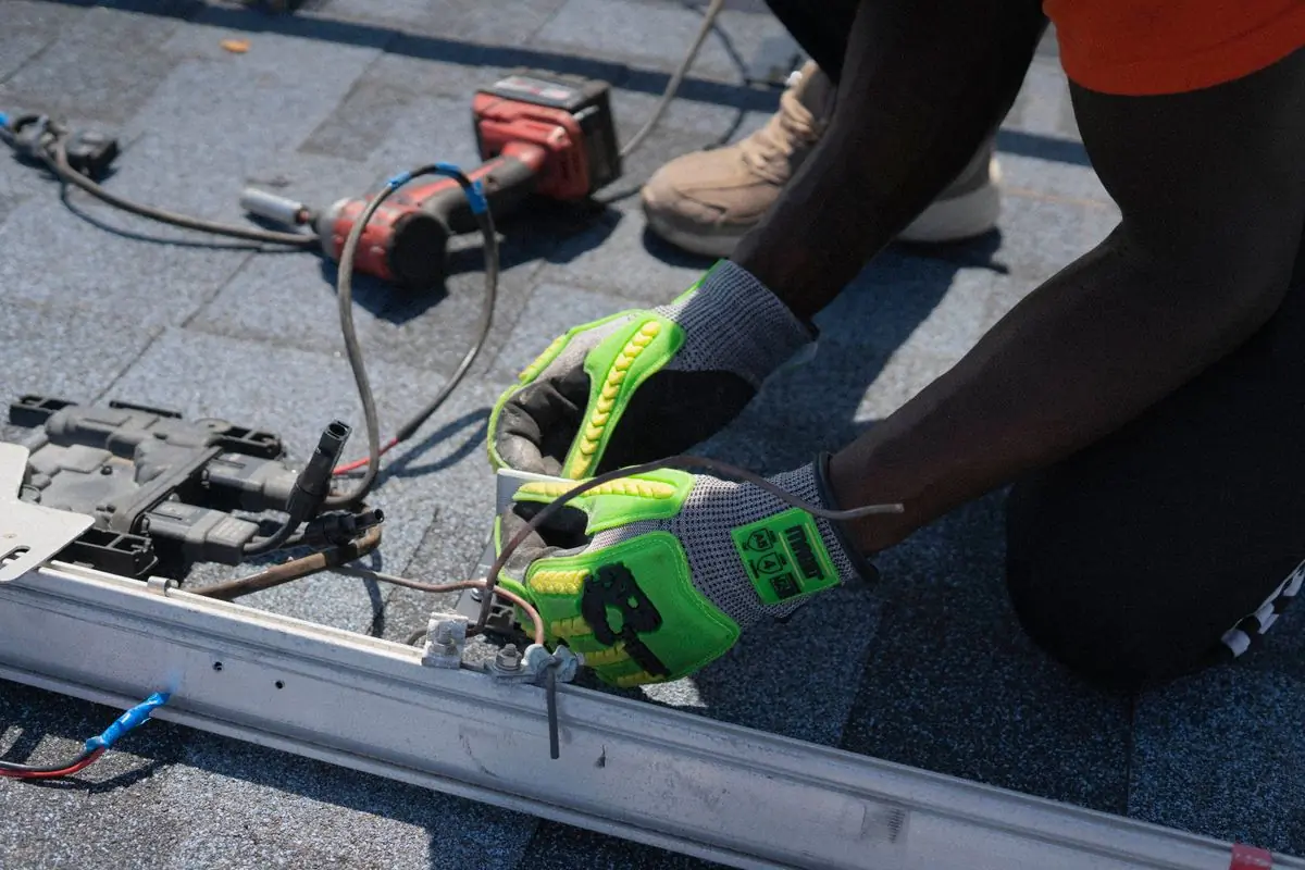 Gloved hands driving a fixing through a mounting rail on a rooftop