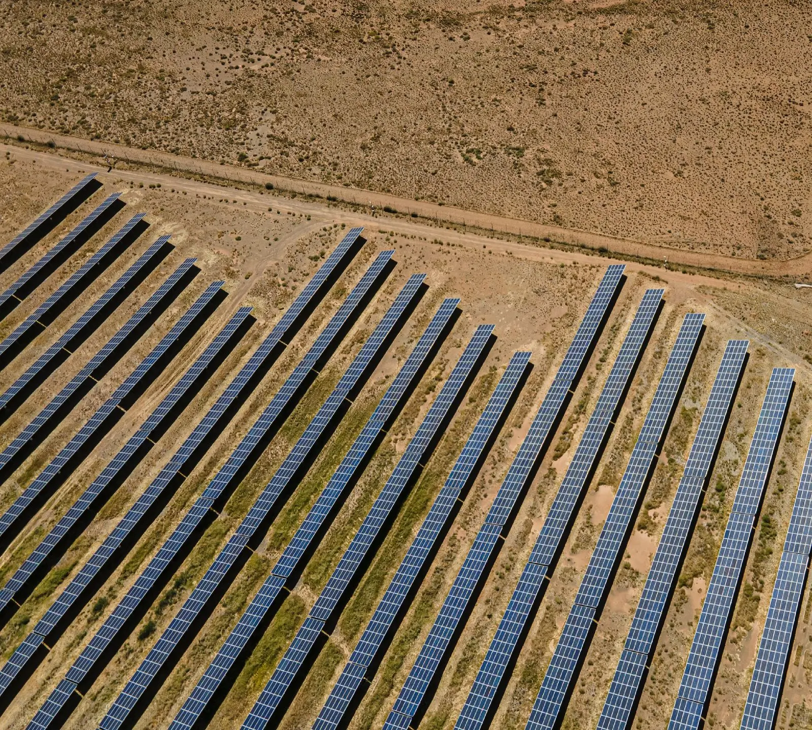 An aerial view of long rows of ground-mounted solar panels in dry open country