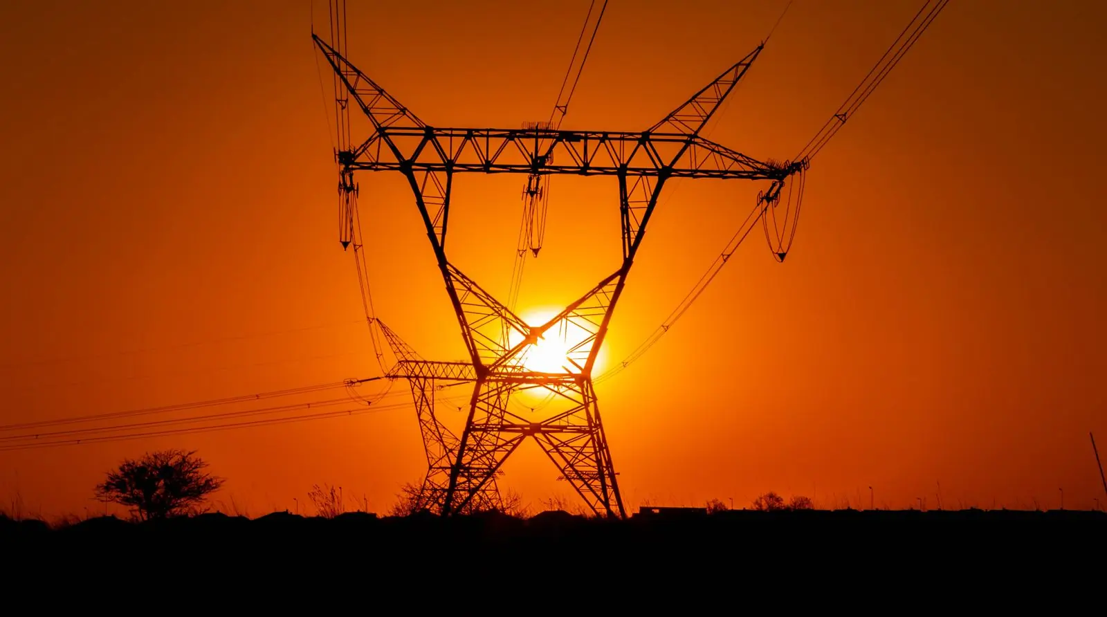 A high-voltage transmission pylon silhouetted against a deep orange sunset