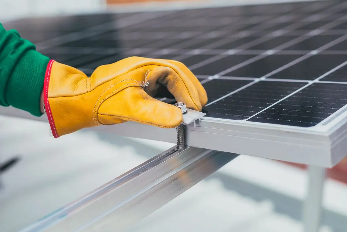 A gloved hand resting on the aluminium frame of a solar panel