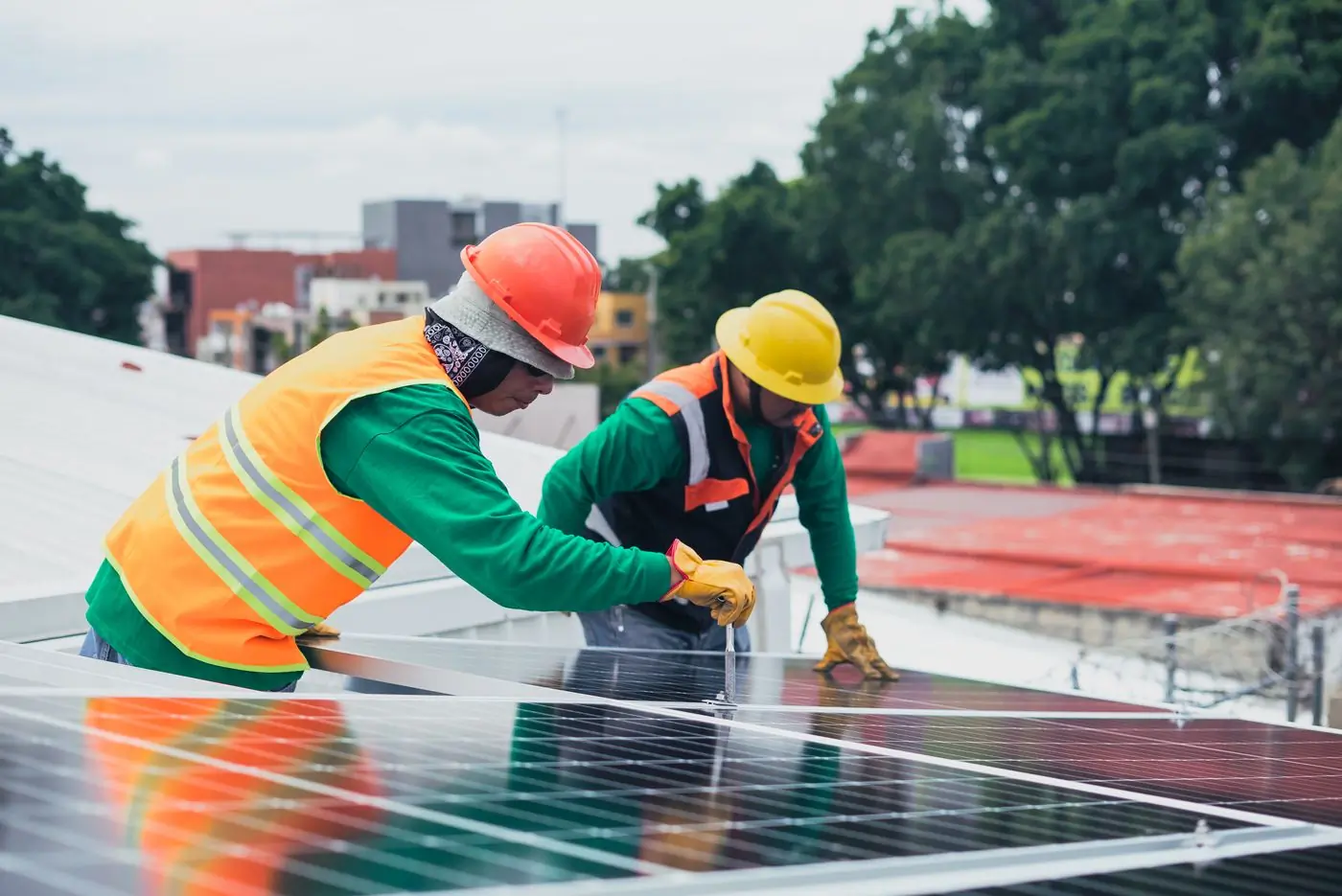 Two installers in hi-vis and hard hats seating a panel onto its rail on a city rooftop