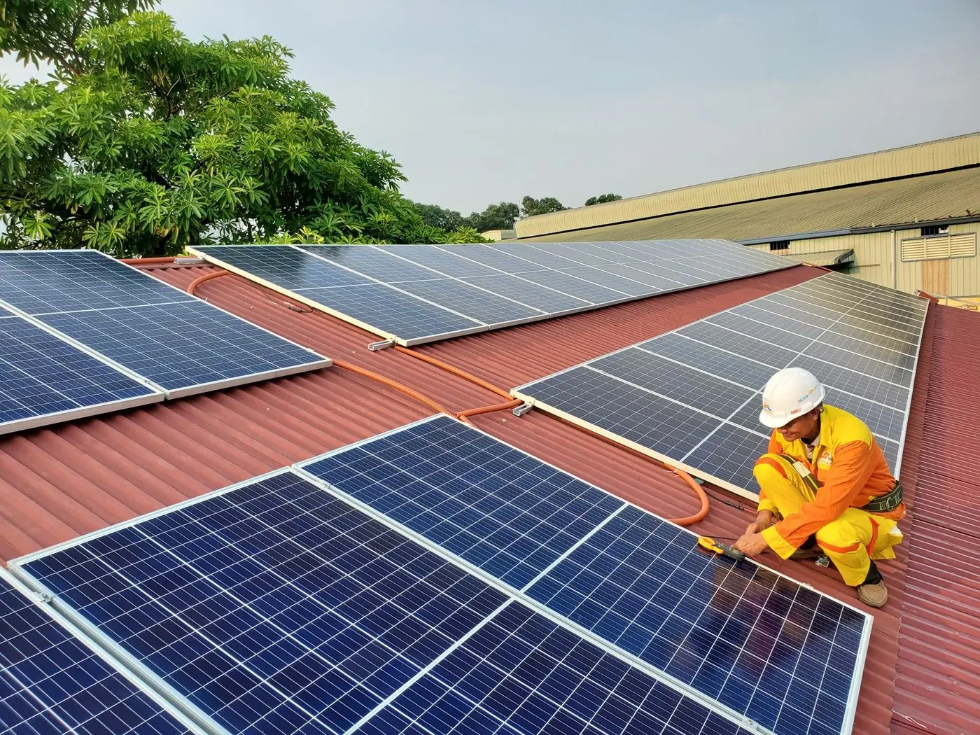 A technician in yellow overalls fixing panels across a red metal roof