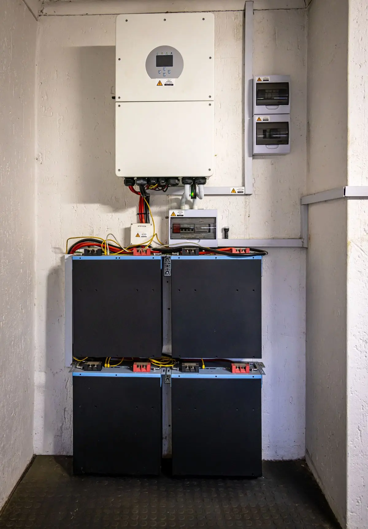 A wall-mounted inverter above four battery modules in a plant room