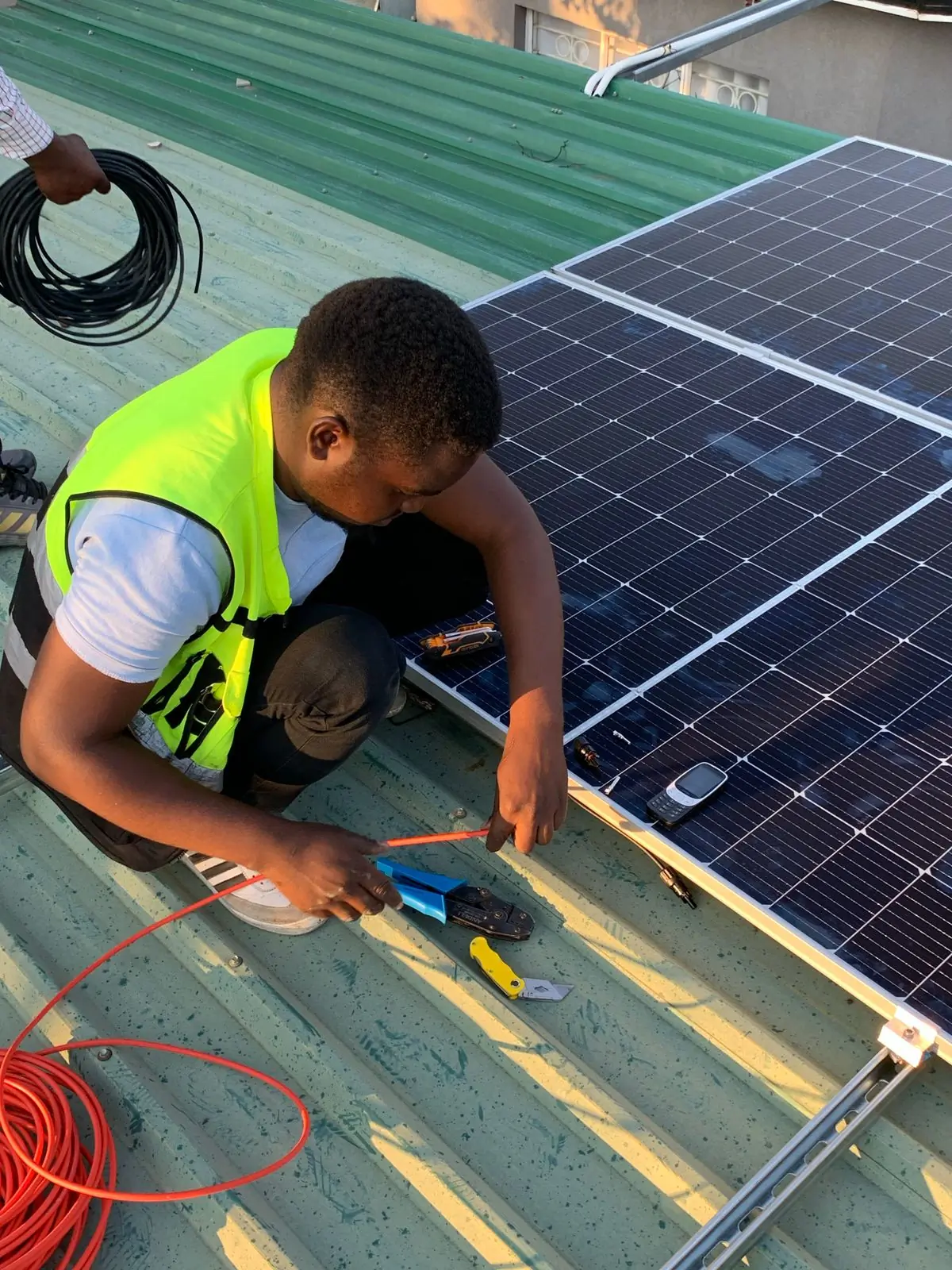 A technician crouching on a roof terminating the cable run from a panel array