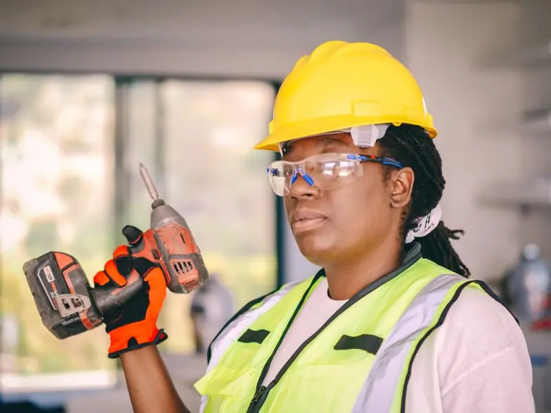 A technician in safety glasses and a yellow hard hat holding a power drill