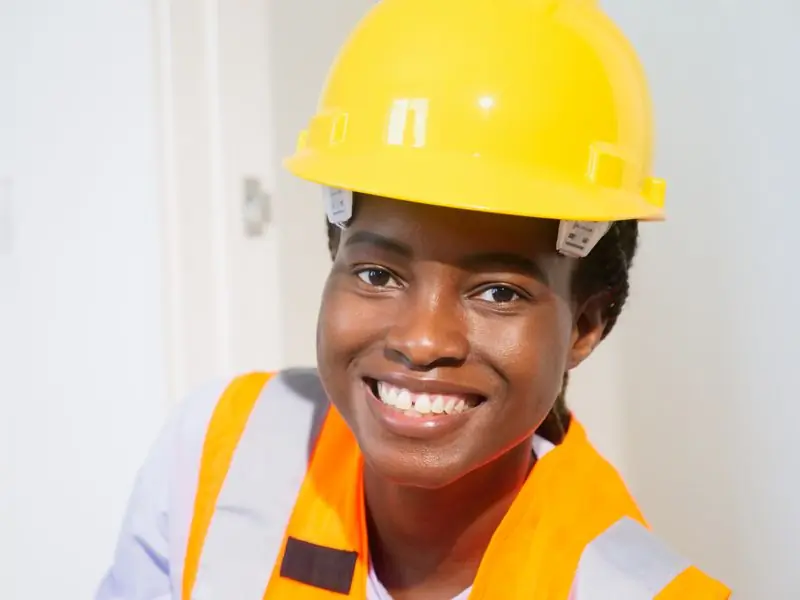 An engineer in a yellow hard hat and high-visibility vest, smiling
