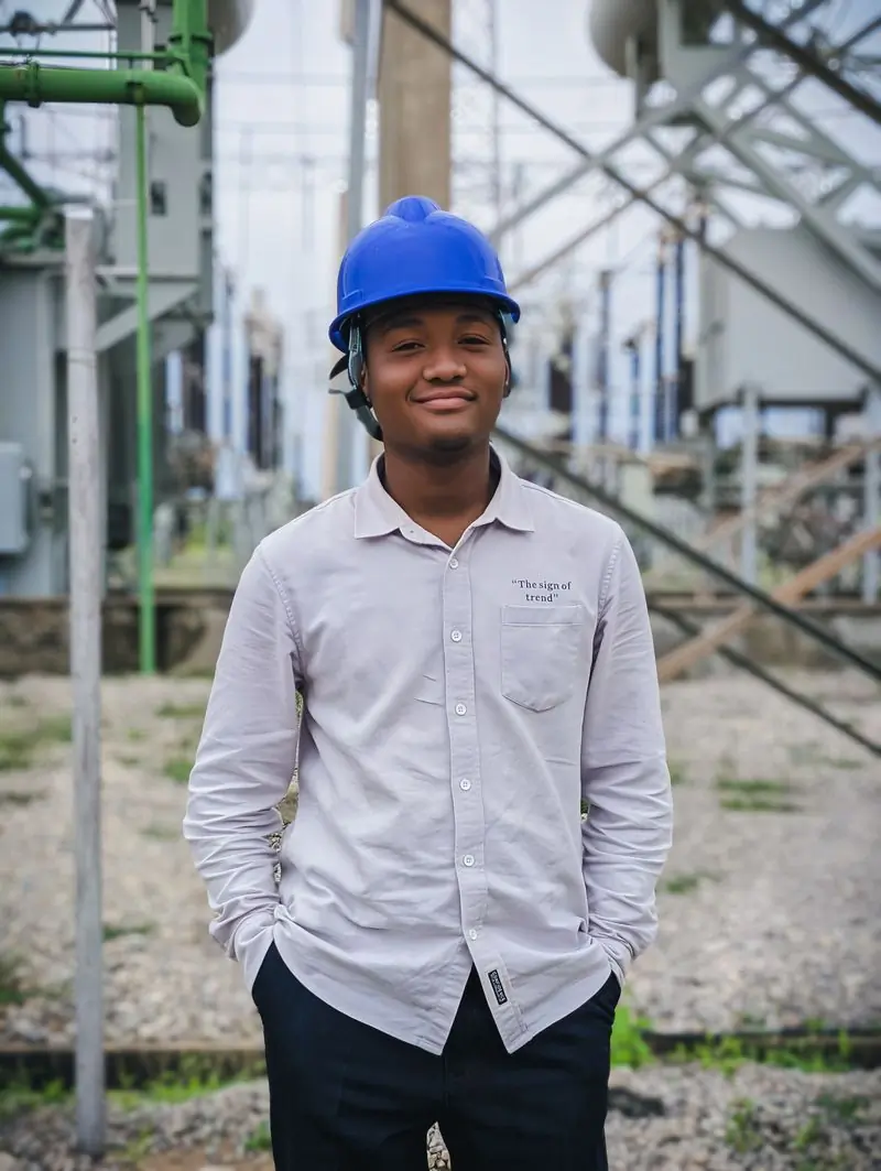 A young engineer in a blue hard hat standing in an electrical substation