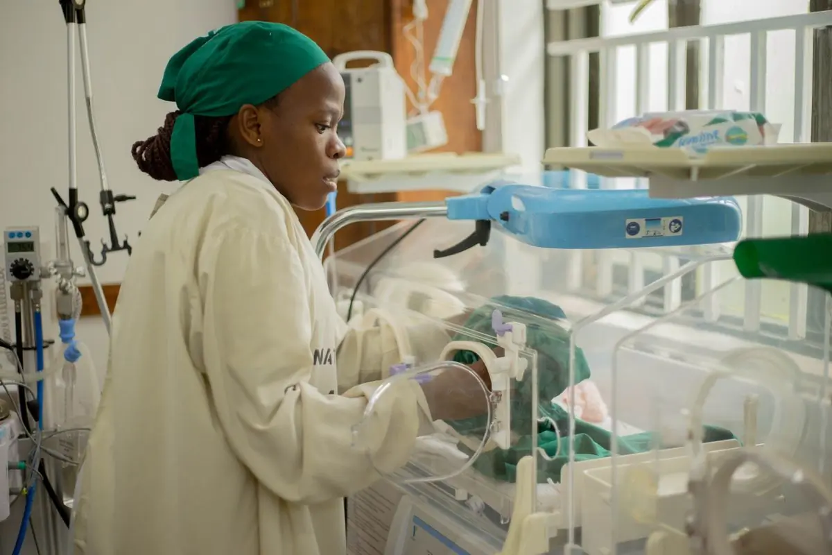 A neonatal nurse checking on a baby in an incubator