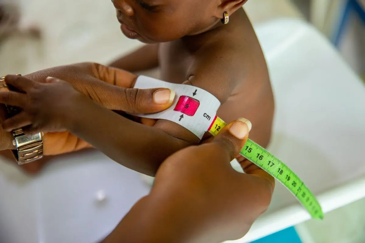 A community health worker measuring a child's arm with a MUAC tape