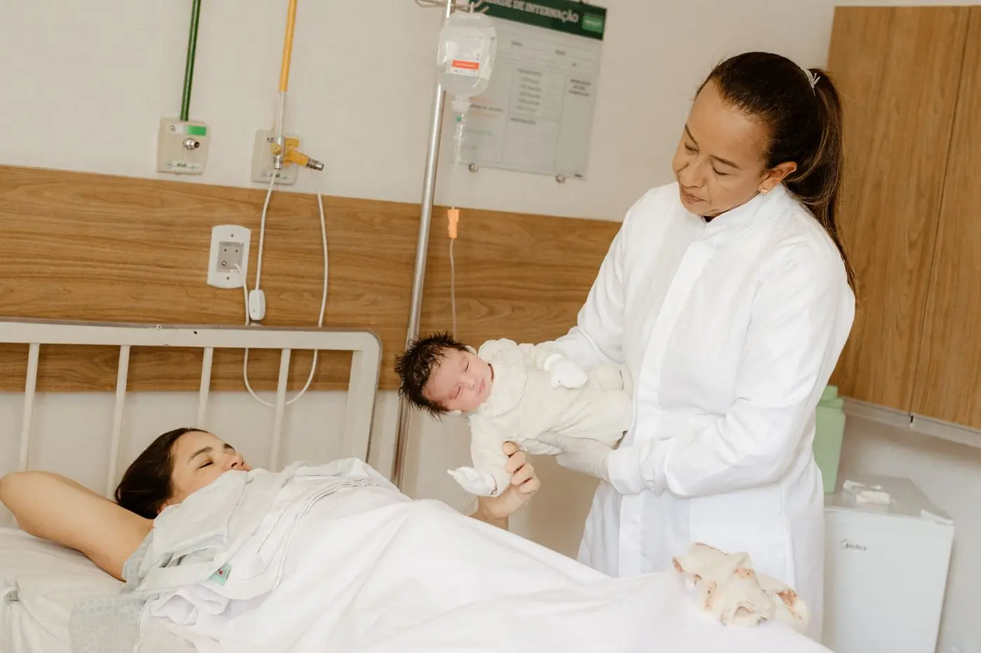 A paediatrician handing a newborn back to her mother on the postnatal ward
