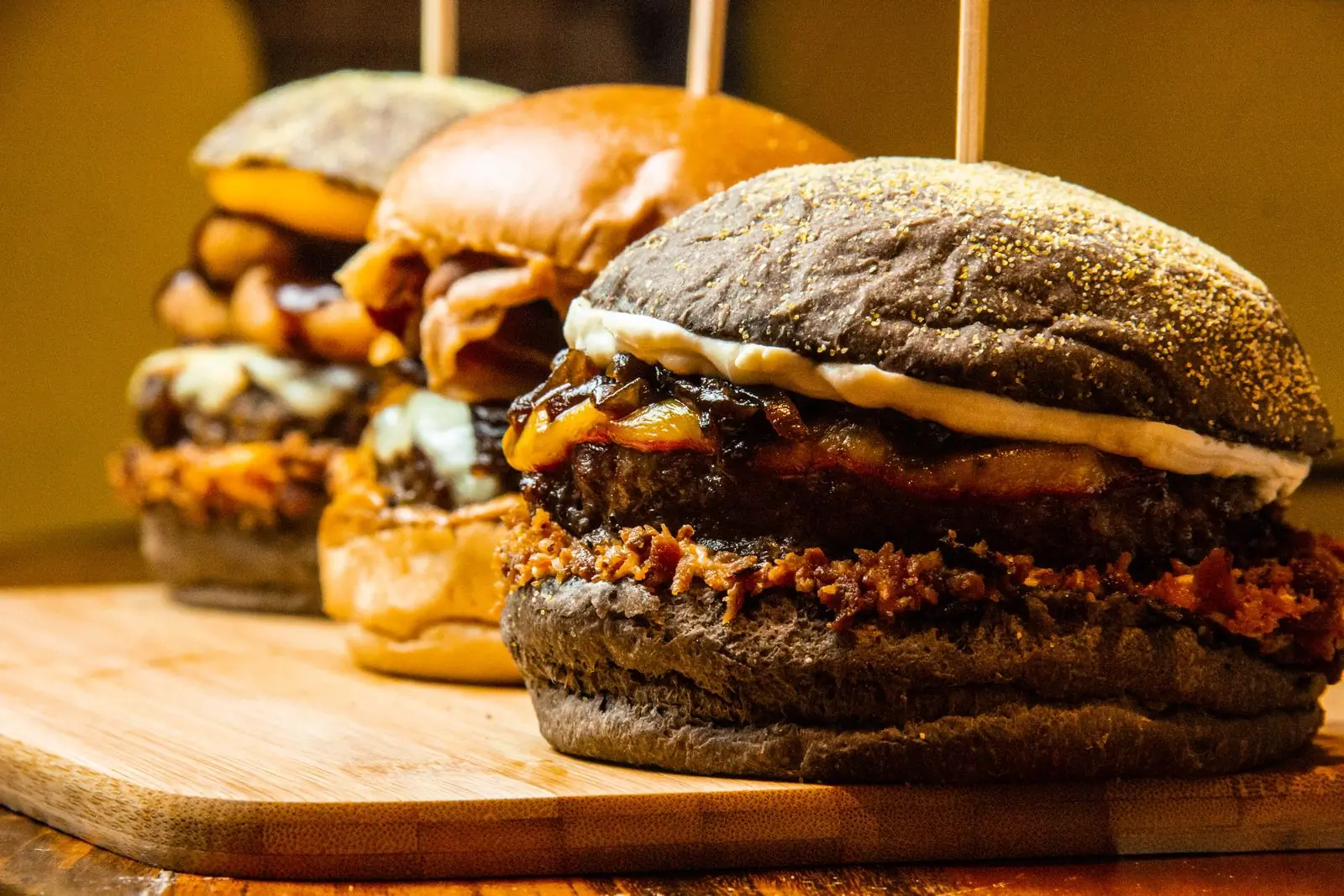 A stack of char-grilled burgers on a wooden board