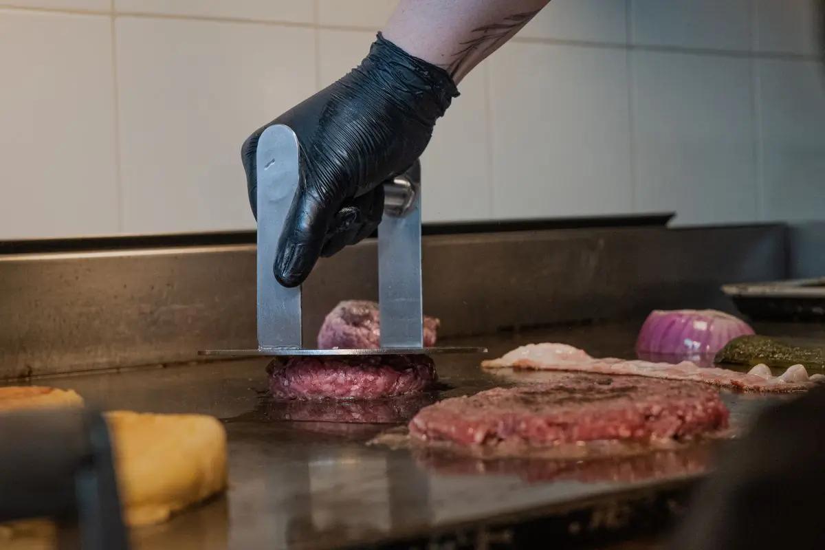 A cook working a burger over the grill