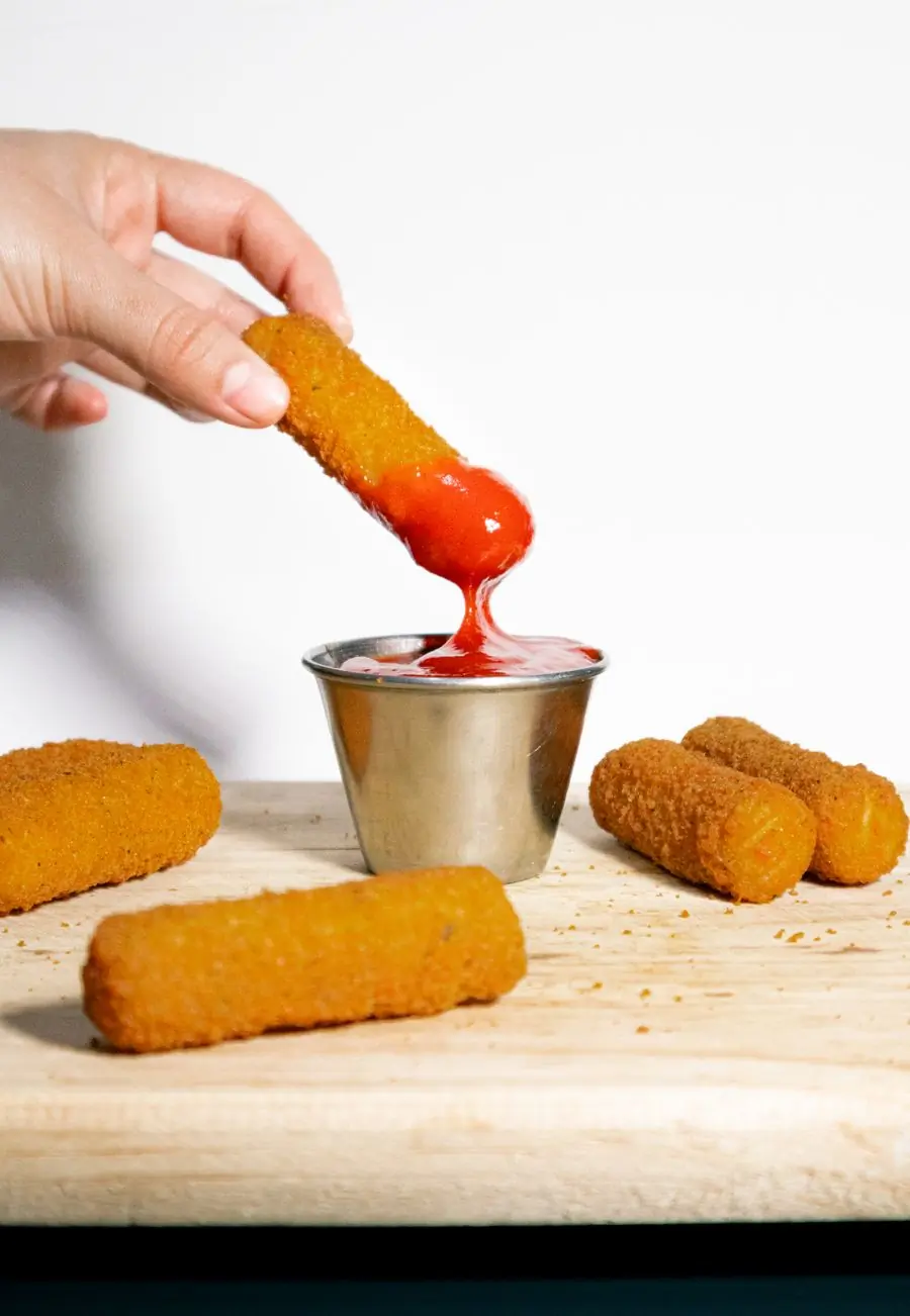 A mozzarella stick being dipped into a pot of sauce