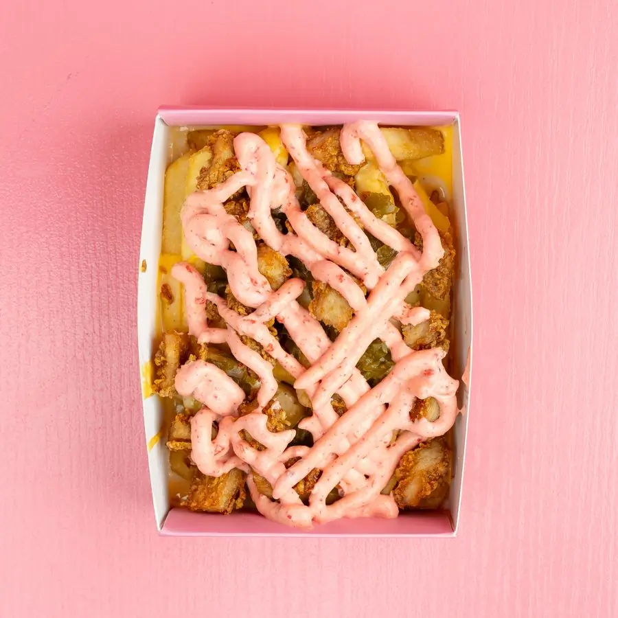 A box of loaded fries under a drizzle of sauce
