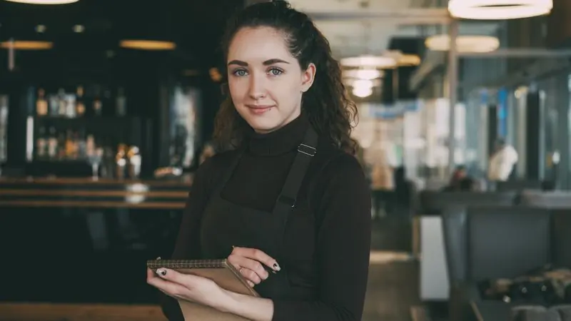 A smiling member of the front-of-house team holding a notepad