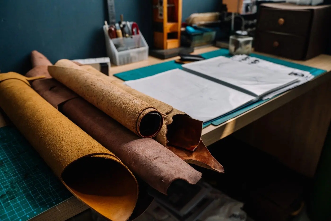 Rolls of tan hide resting beside pattern sheets on a cutting bench