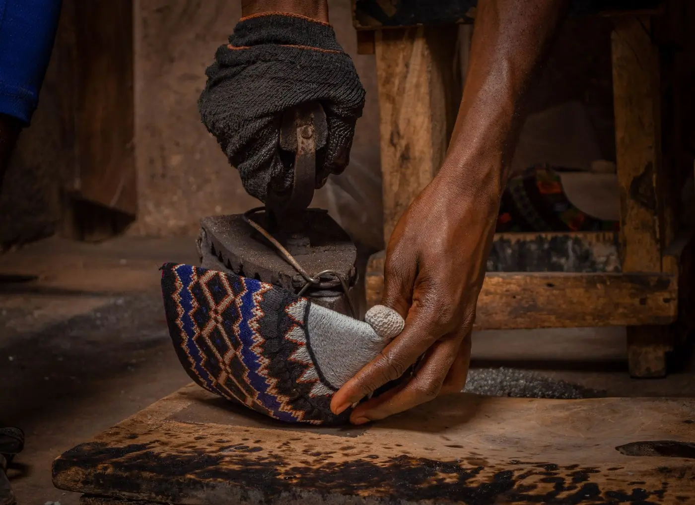 An artisan's hands shape a patterned shoe over a wooden last on a worn bench