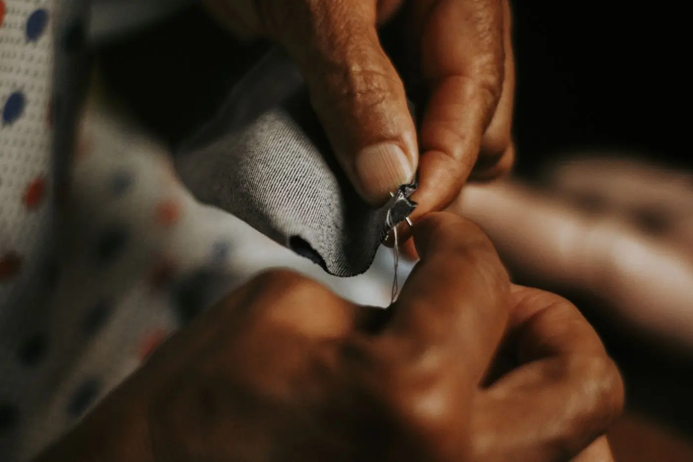 Close up of hands drawing a needle through grey cloth in low warm light