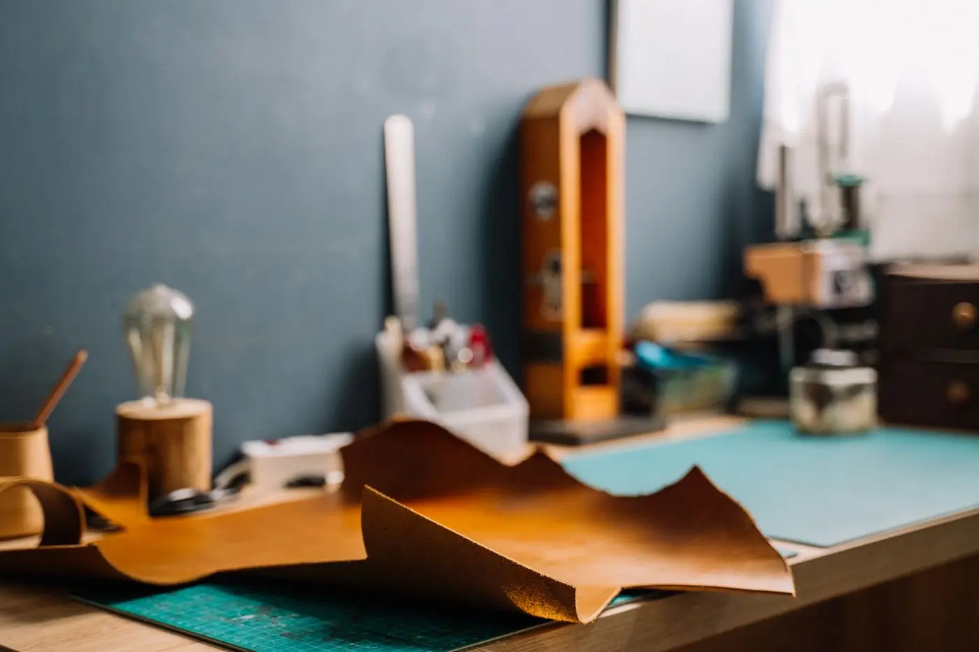 Cut sheets of tan leather and hand tools laid out on a workshop table