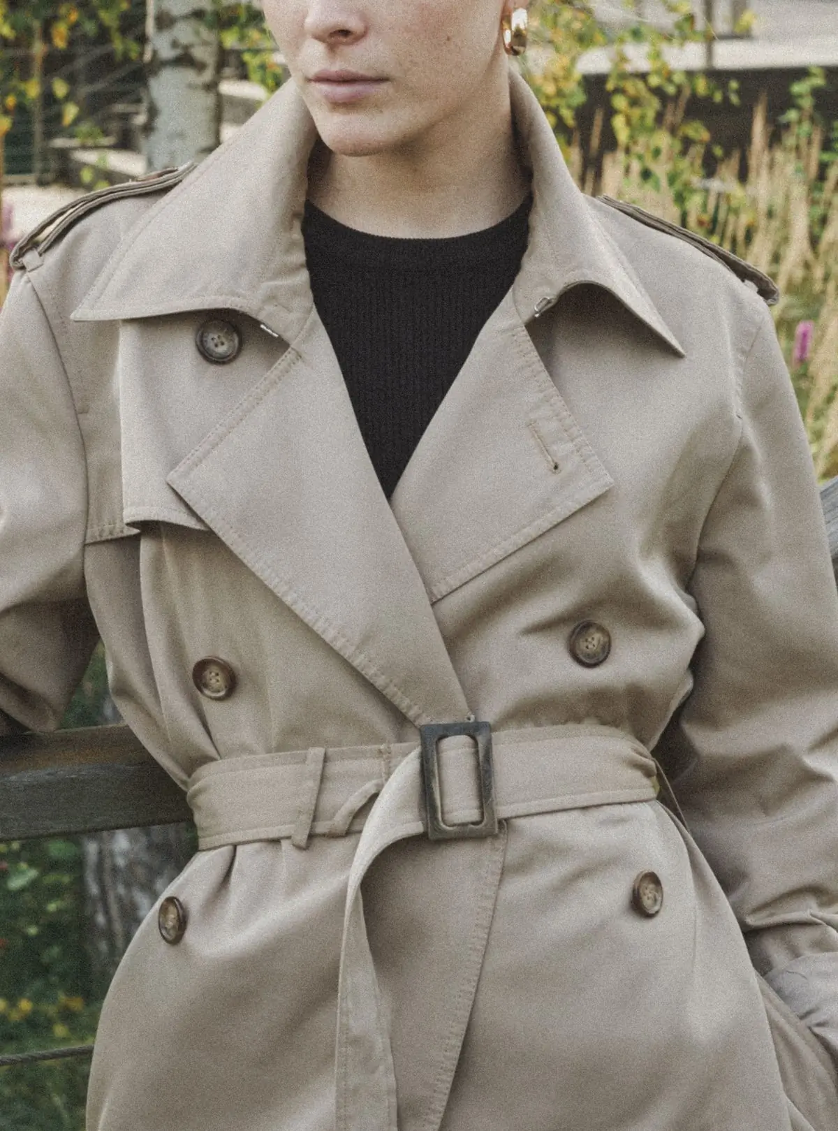 The buttoned front and tied belt of a stone trench coat, close up