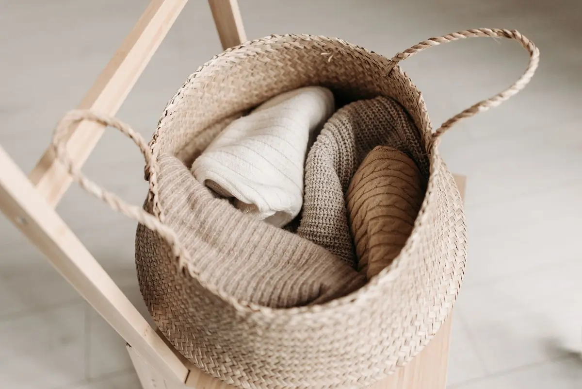 Cream and camel knits rolled into a woven basket on a light wooden stand