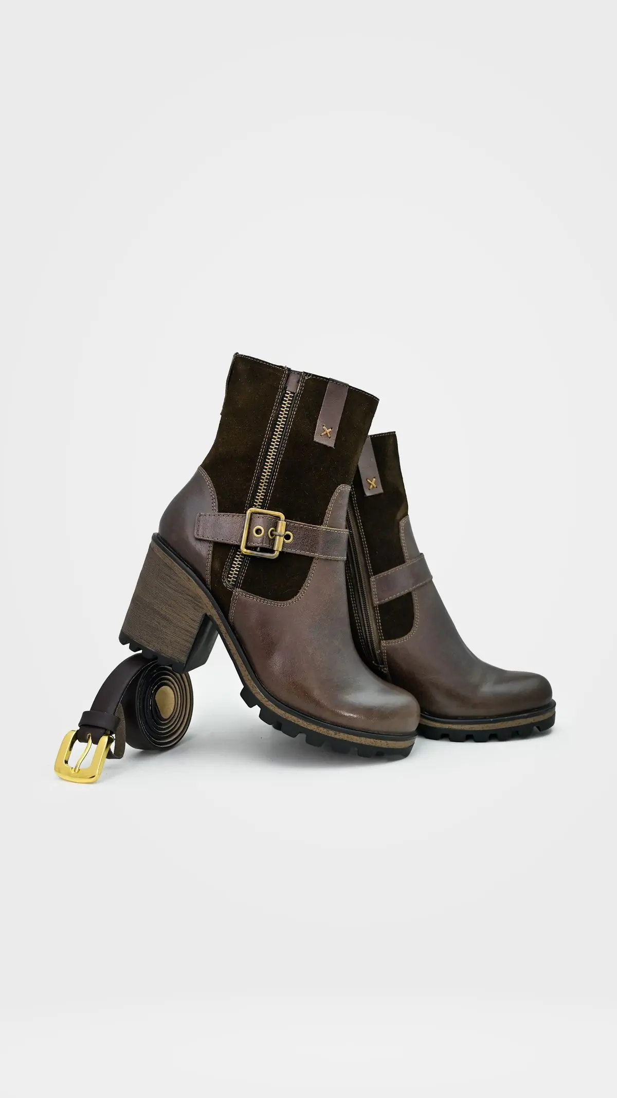 A brown leather and suede ankle boot with a brass buckle on a stacked heel