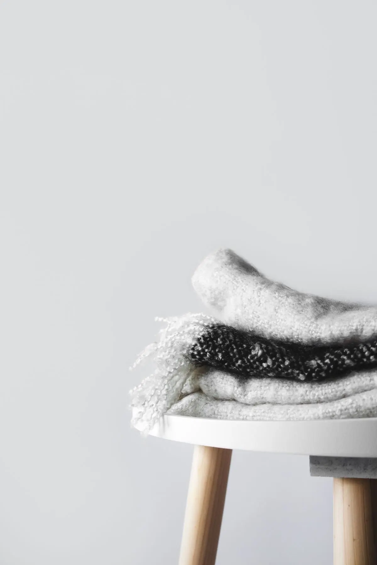 Folded wool scarves stacked on a round table against a bare white wall
