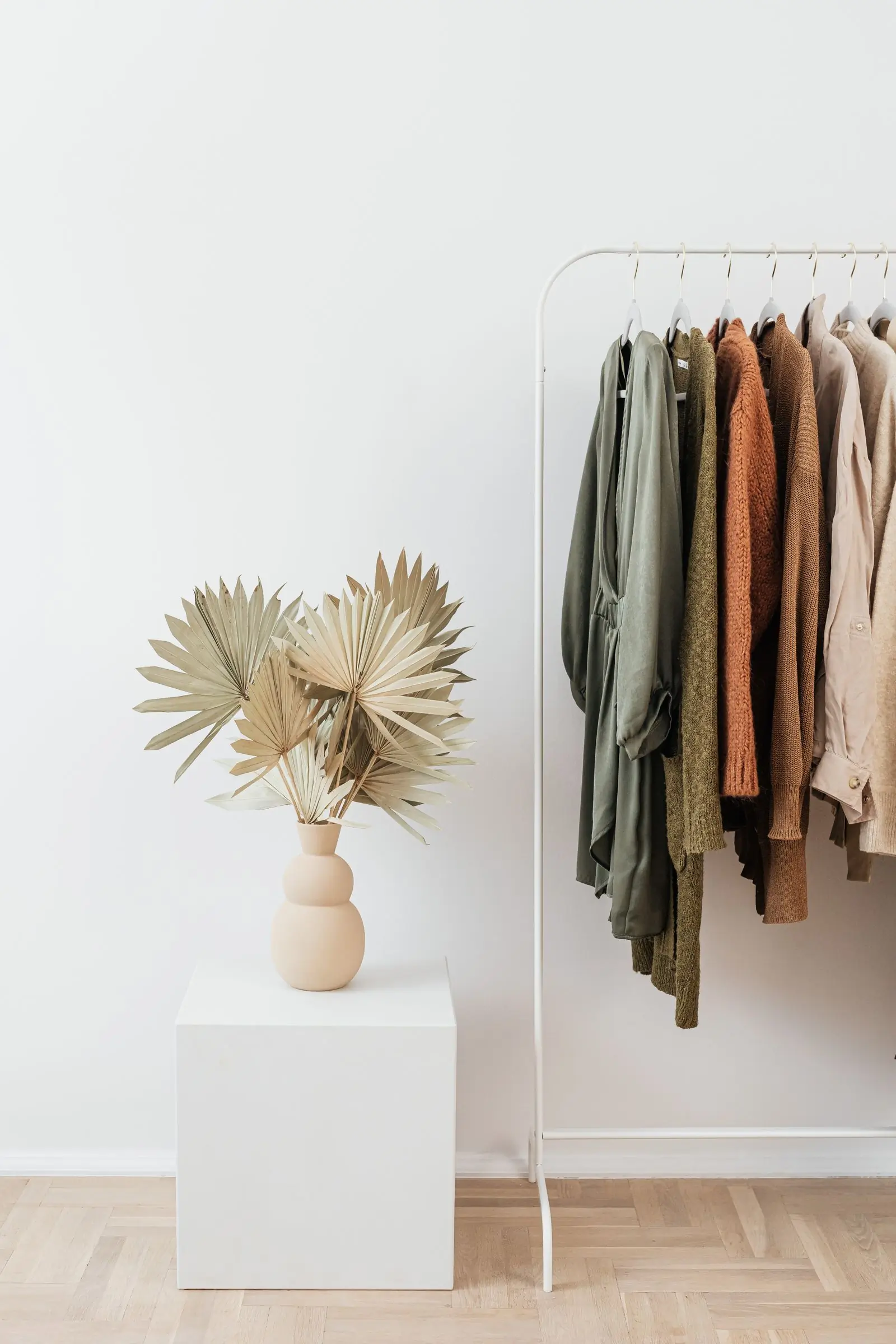 Dried palm fronds in a stone vase beside a rail of olive, rust and cream garments
