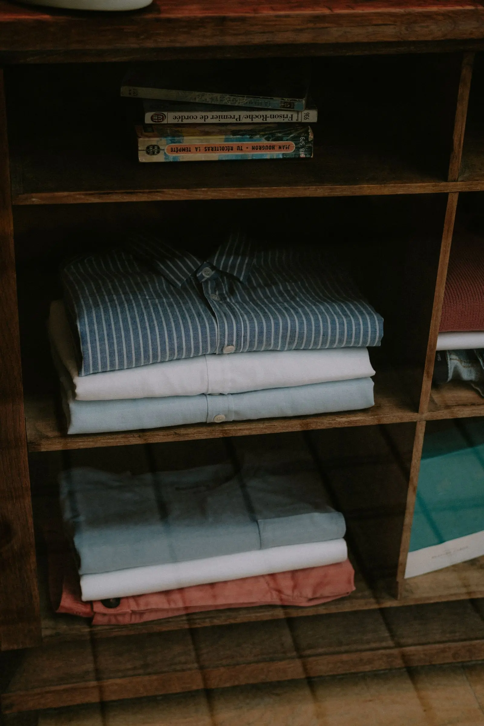 Folded shirts stacked on a dark wooden shelf in soft indoor light