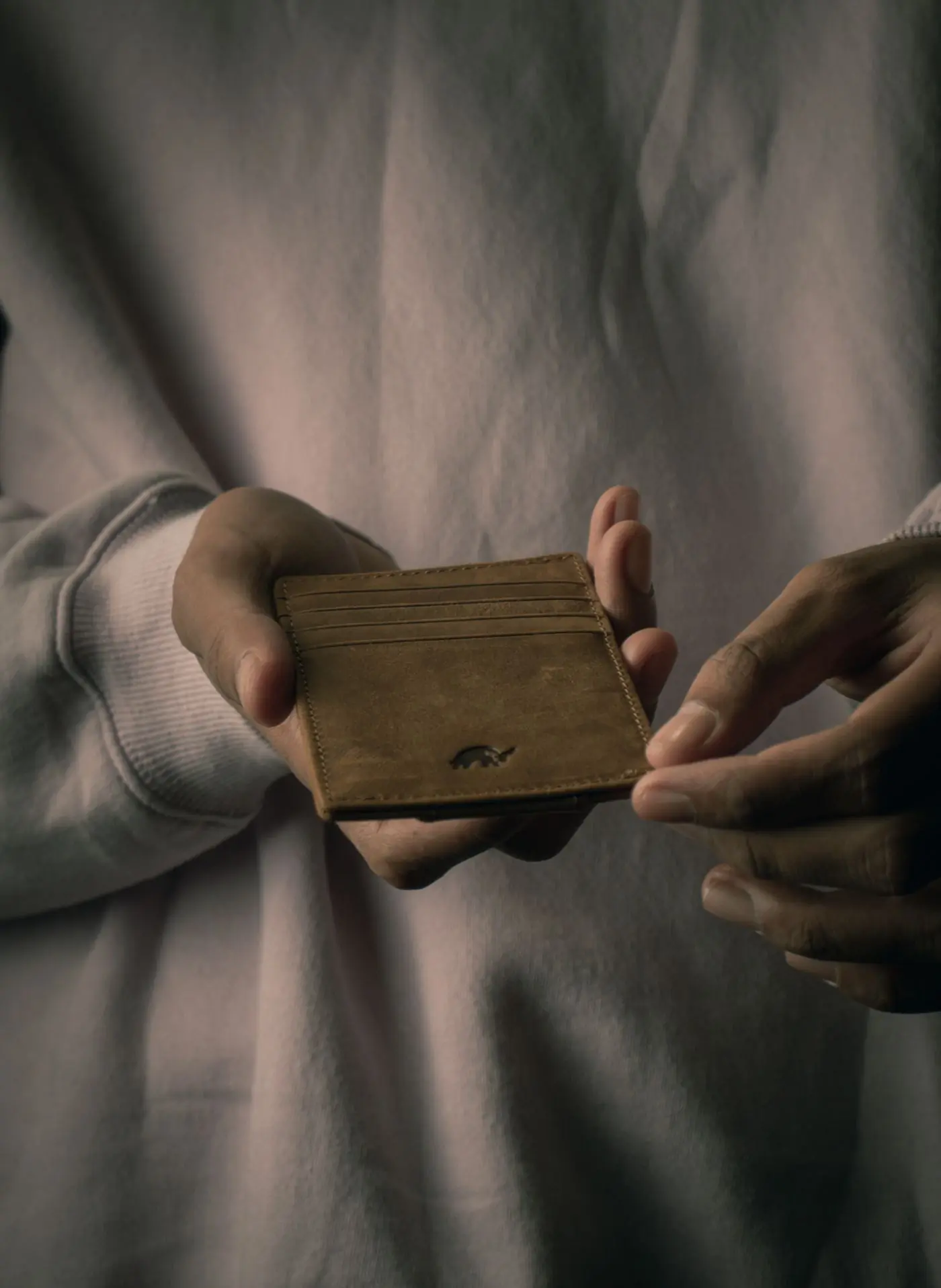 Two hands hold an olive suede card holder open against a grey knit sleeve