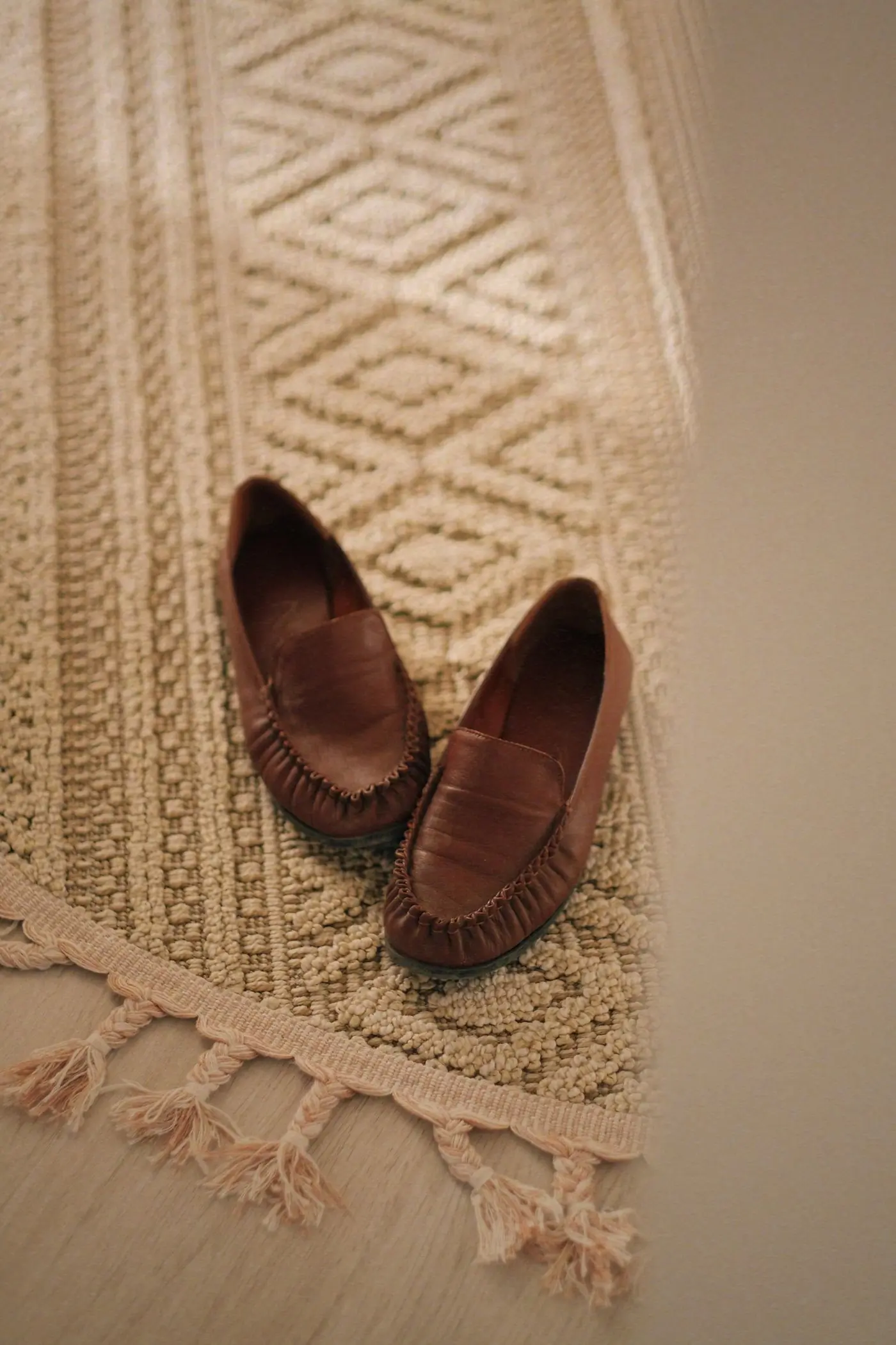 A pair of soft brown leather loafers resting on a cream woven rug