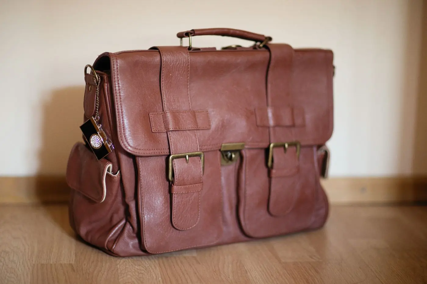 A soft brown leather weekend bag with brass buckles standing on a wooden floor