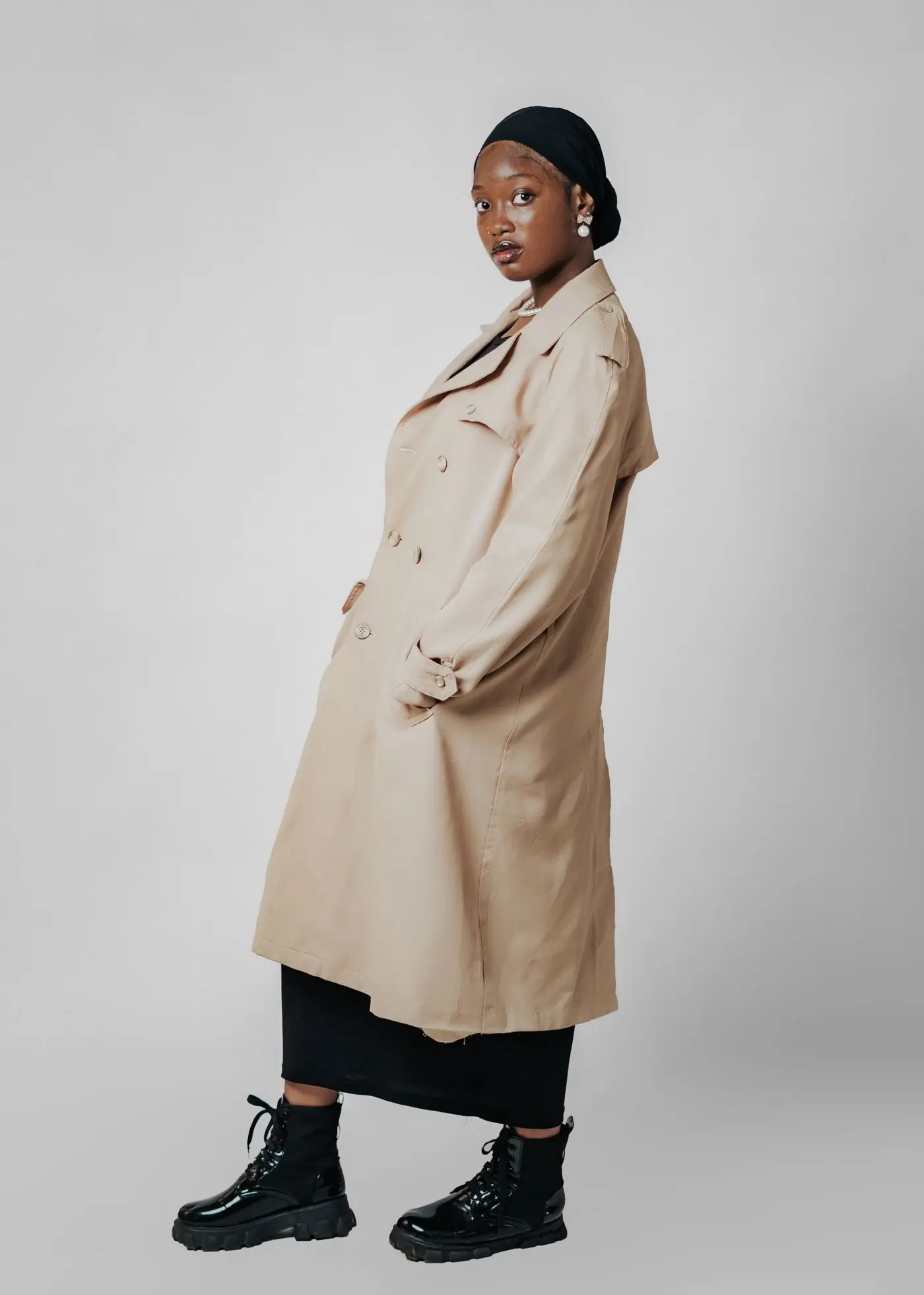 The sleeve and storm flap of a stone-coloured trench coat against a plain wall