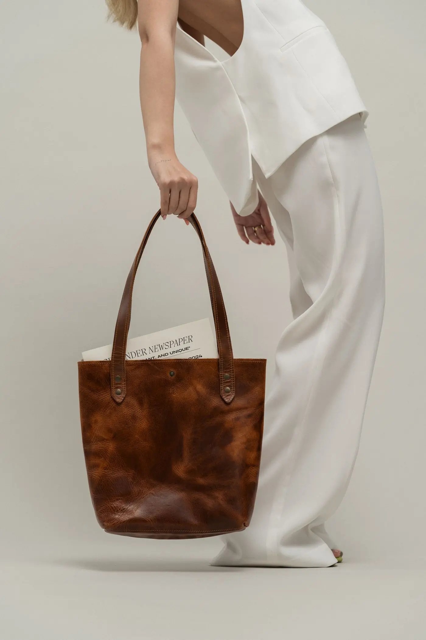 A tan leather tote carried at the side against soft white cloth