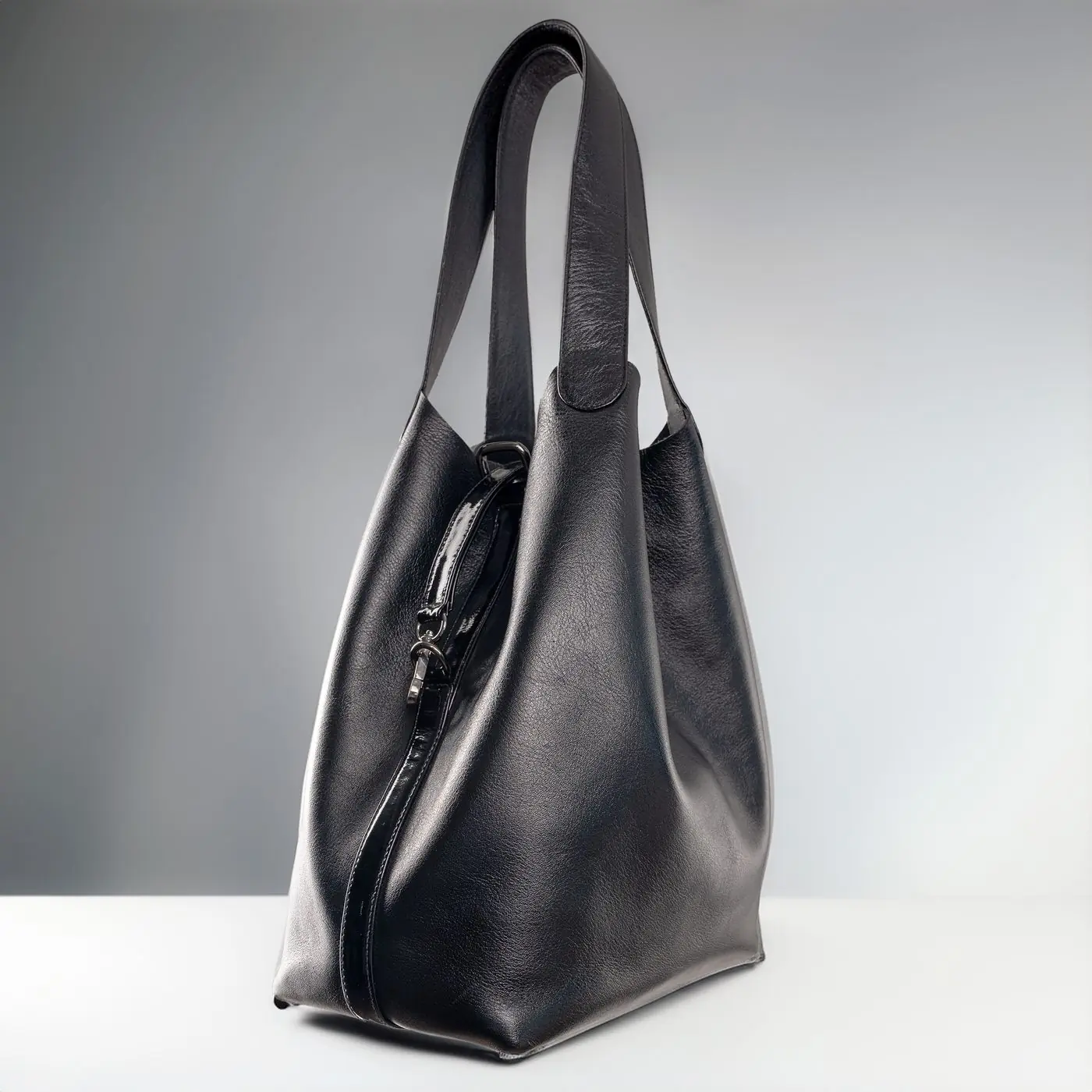 A slouched black leather shoulder bag suspended against a pale grey ground