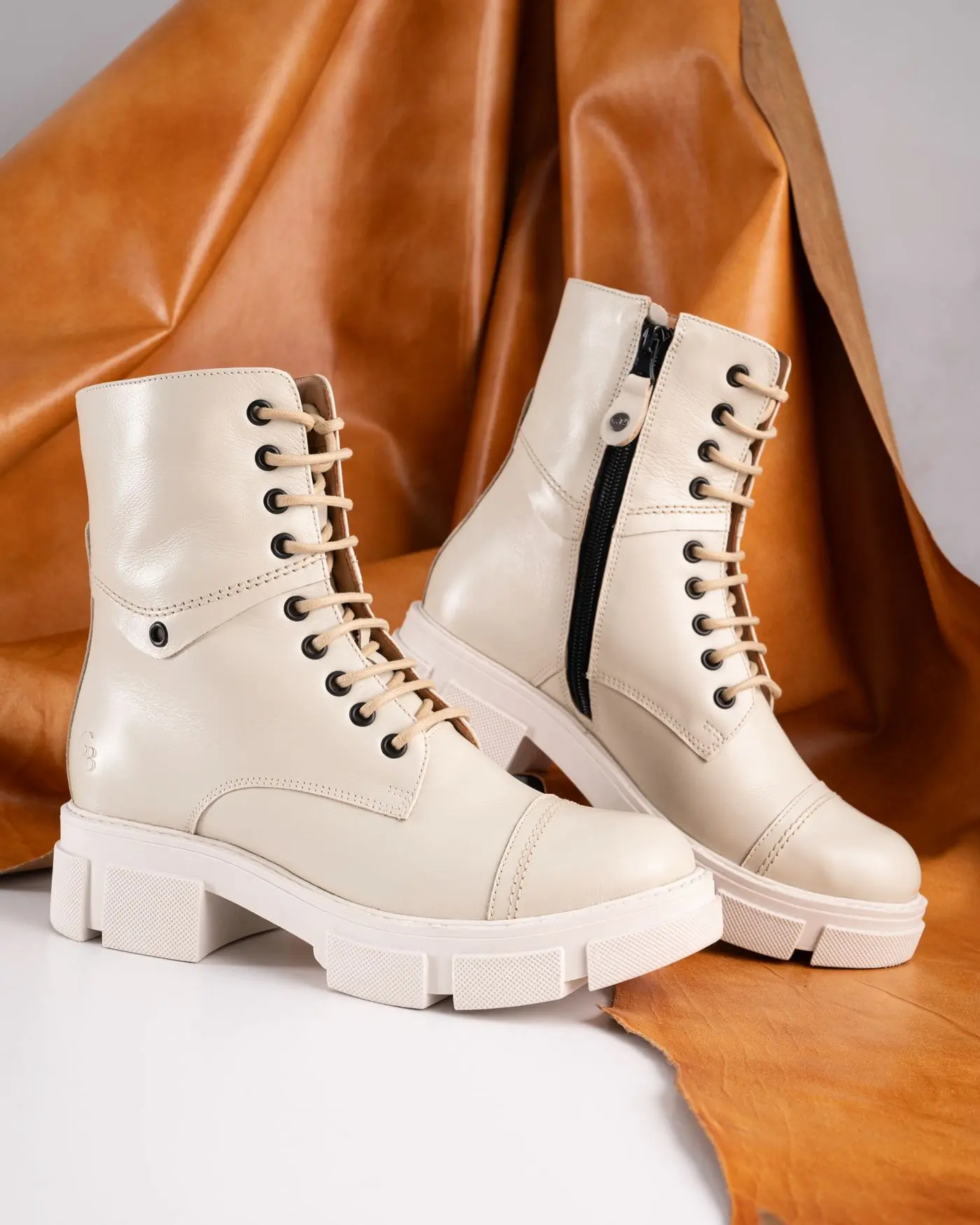 A pair of cream leather lace-up boots standing on a fold of tan hide