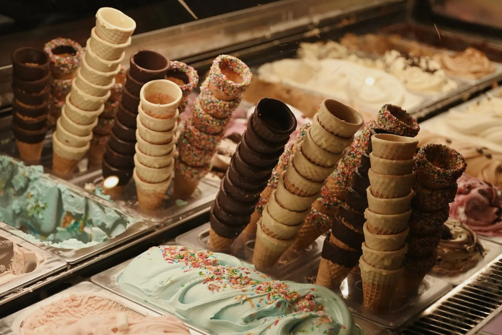 Waffle, chocolate-dipped and sprinkle-rimmed cones standing in a lit glass case above pans of mint ice cream