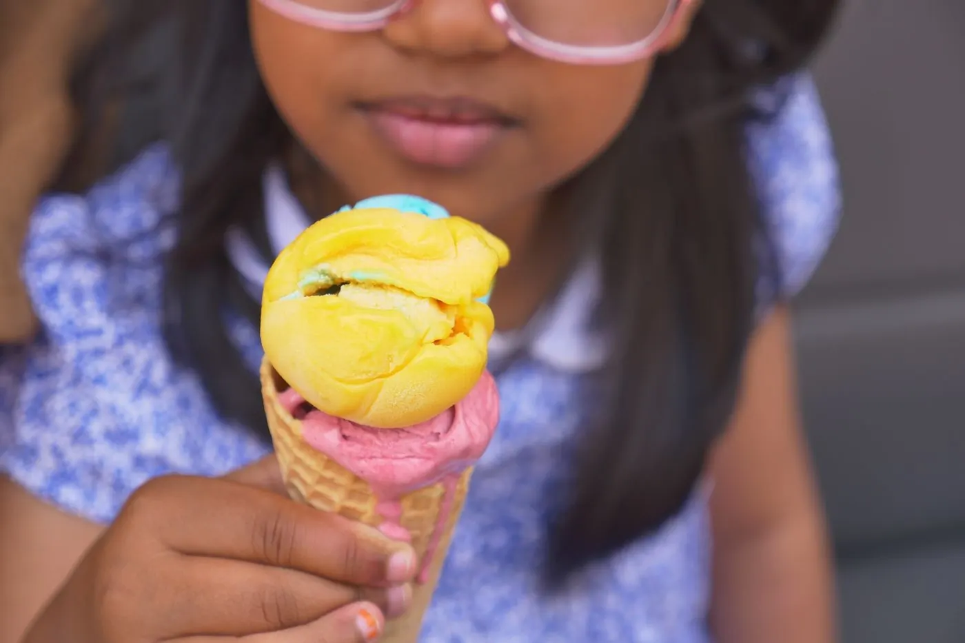 A woman laughing over a cone of soft ice cream against a clear blue sky