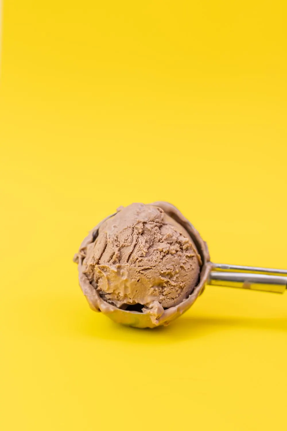 Two dark chocolate scoops stacked in a waffle cone against a plain wall