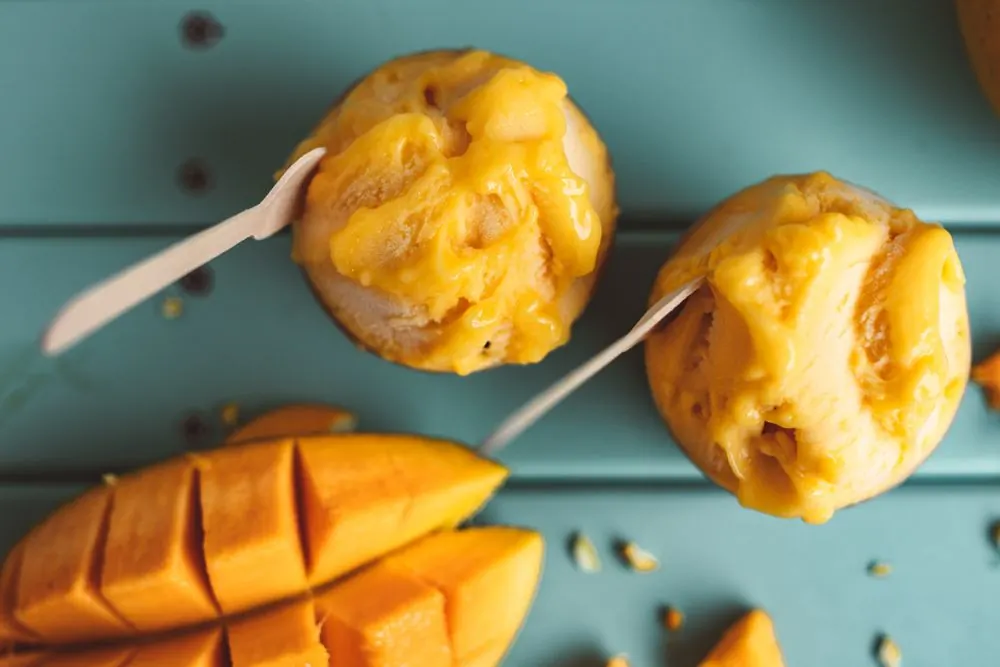 A bright orange mango sorbet scoop in a cone, sunlit from the left