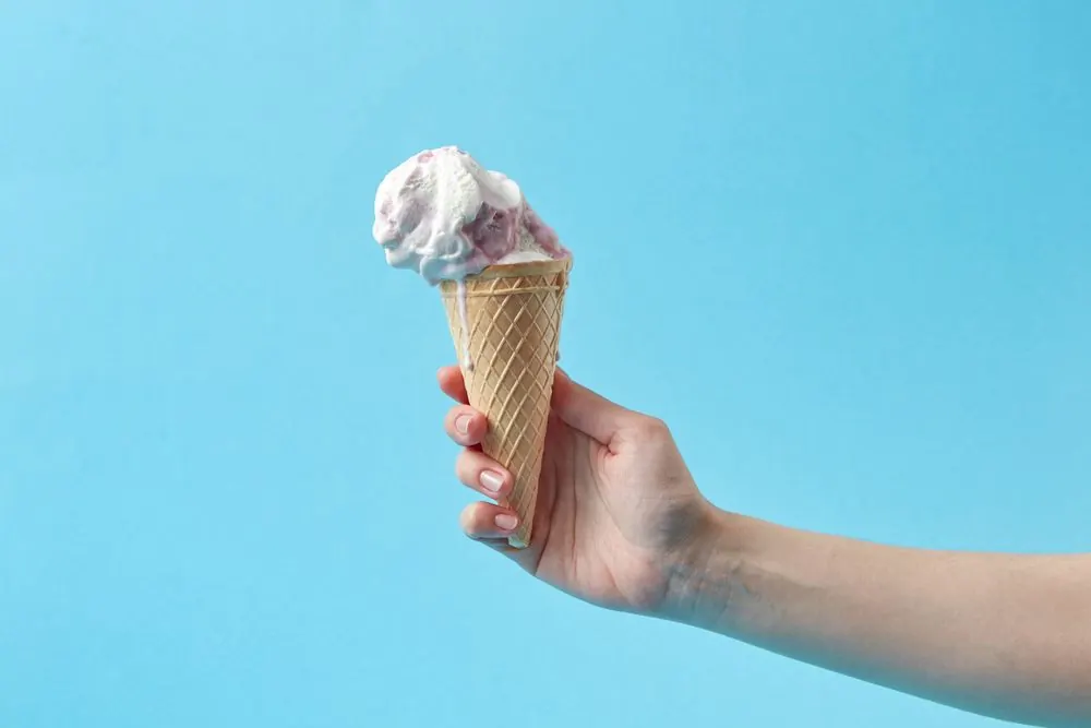 A pale cream scoop of tigernut ice cream curling out of a metal scoop