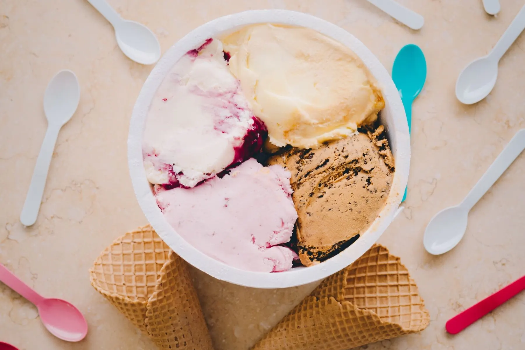 Tubs of ice cream and waffle cones arranged on a pale cream ground, shot from above